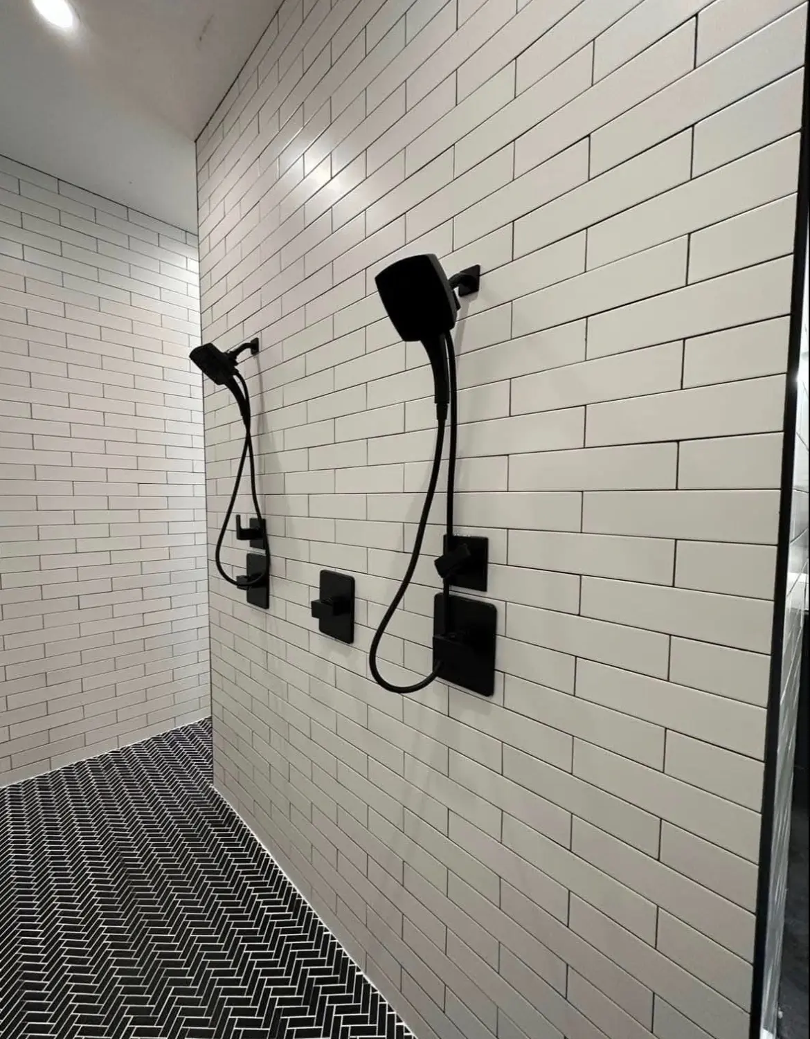 Walk-in shower with white tile walls, black herringbone floor and dual black shower heads